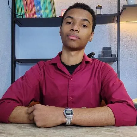 Ryan Zinedine, de camisa vinho, sentado a uma mesa de trabalho